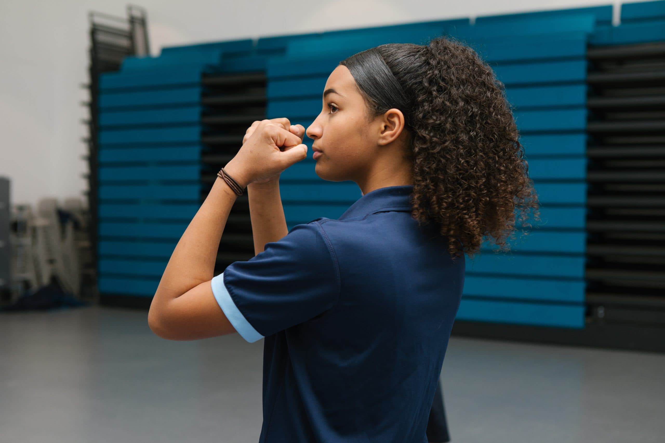 Secondary school girl in a PE uniform practicing a combat stance during a Studio You lesson in a gym