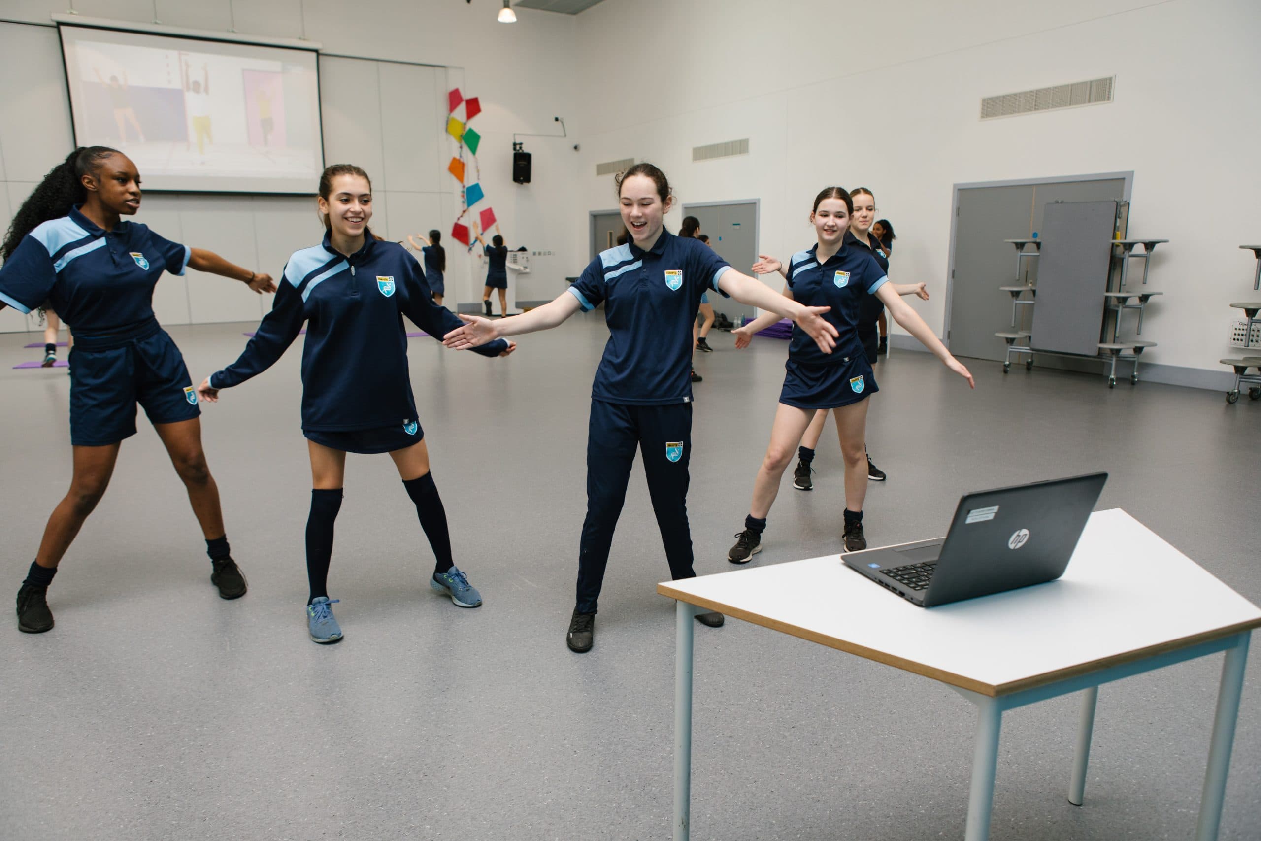A group of teenage girls dancing in front of a laptop within a PE class