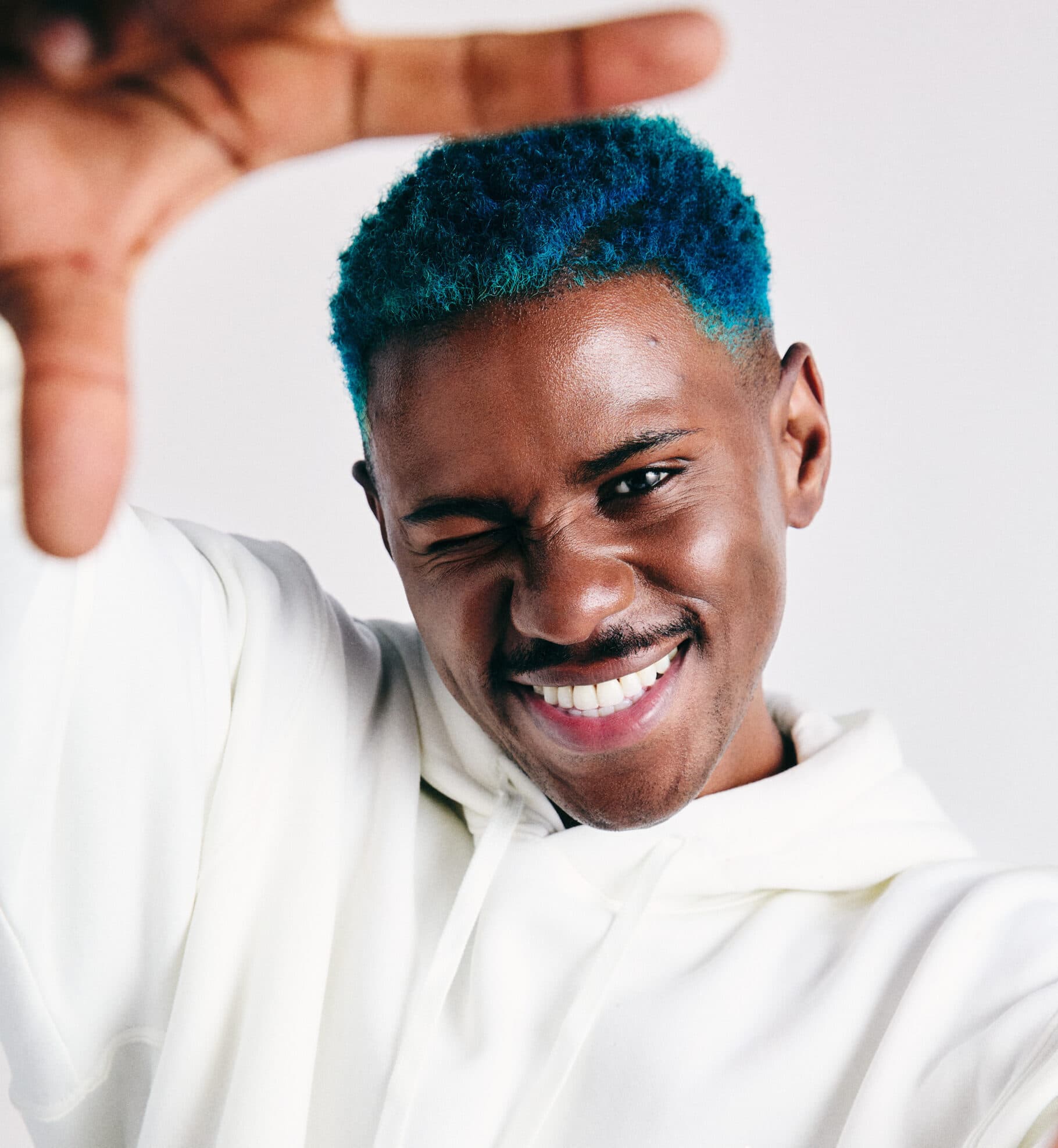 An image of fitness trainer Joelle. A man with short blue hair, wearing a cream hoodie