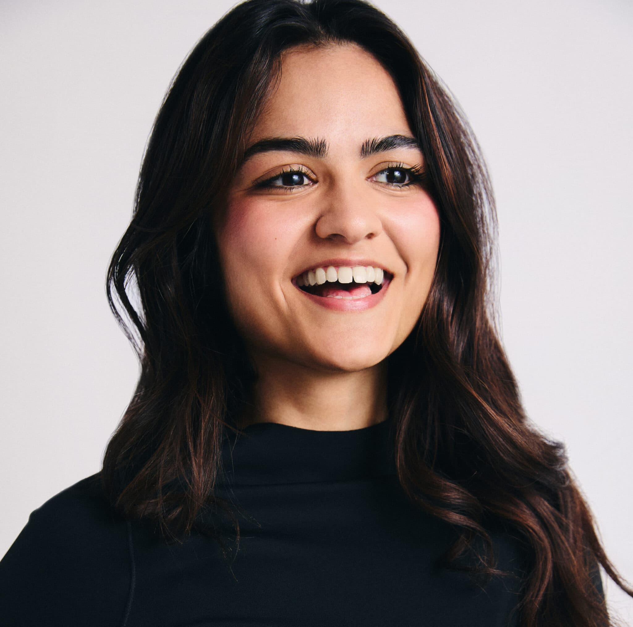 An image of mental fitness trainer, Maya. A woman with long dark brown hair, wearing a black high neck top