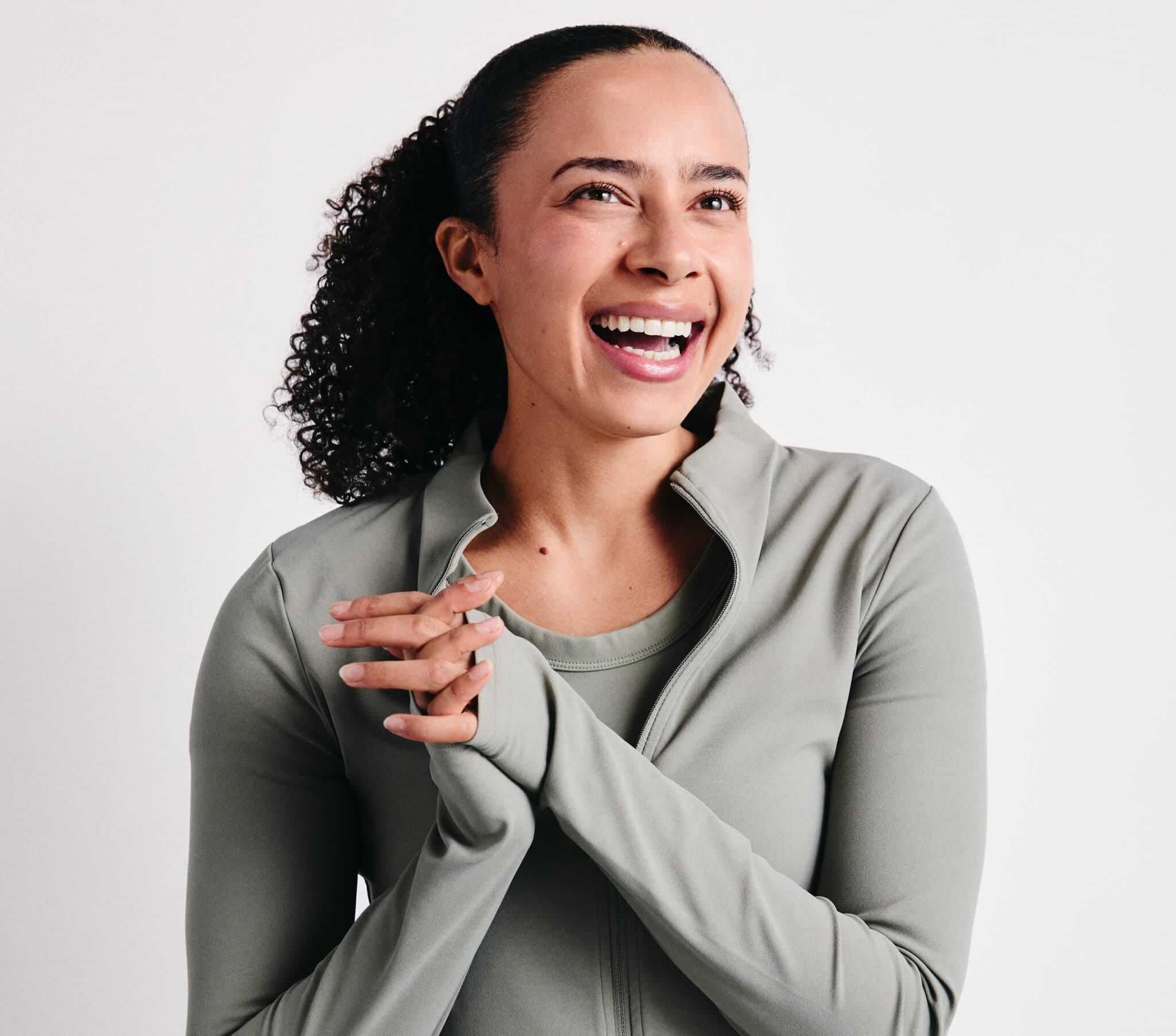 An image of breathwork trainer Rebekah. A woman with black curly hair tied back, wearing a pale green zip up top