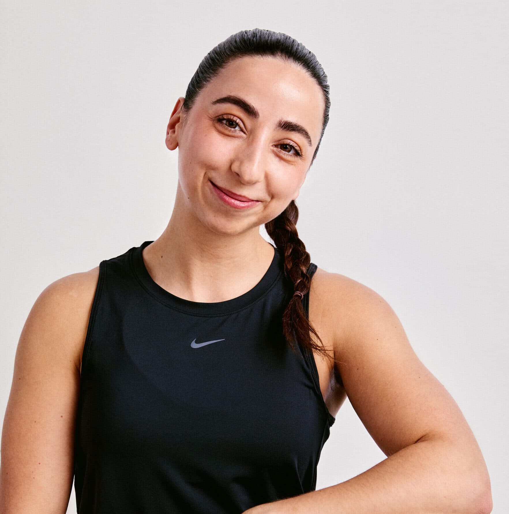 An image of strength trainer Alix. A woman with dark brown hair, tied back in a plait, wearing a black vest top