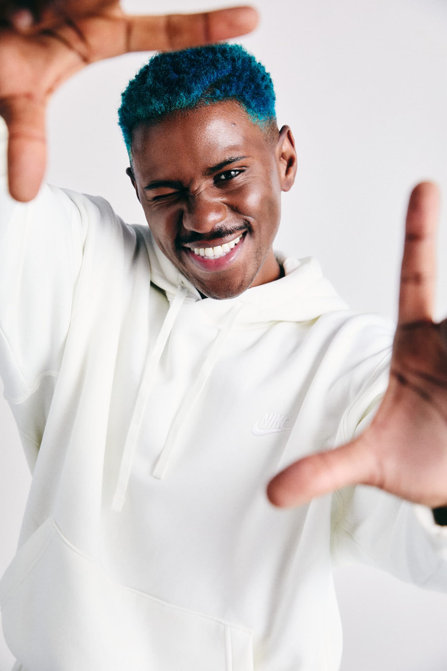 An image of fitness trainer Joelle. A man with short blue hair, wearing a cream hoodie